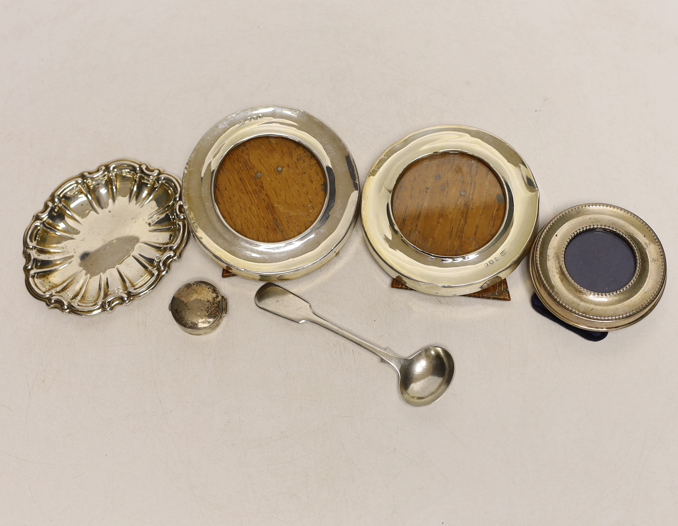 A small pair of George V silver mounted circular photograph frames, London, 1921, 75mm and four other items including a silver pill box and condiment spoon and small frame.
